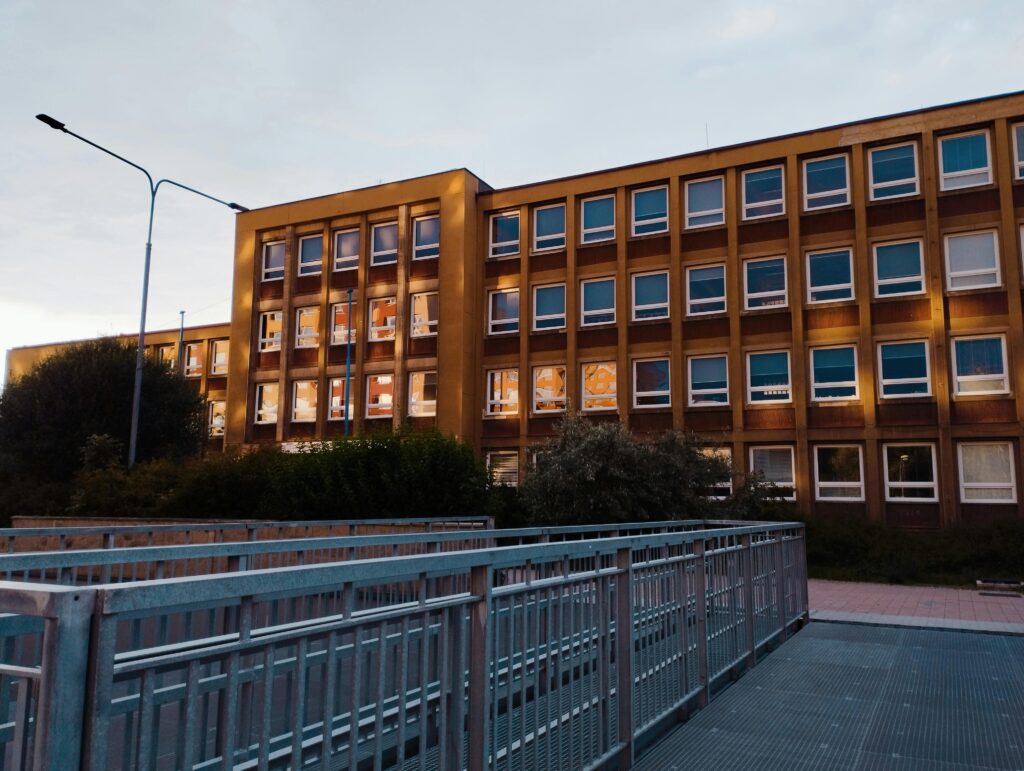 A modern school building facade illuminated at twilight with a pedestrian walkway in the foreground.