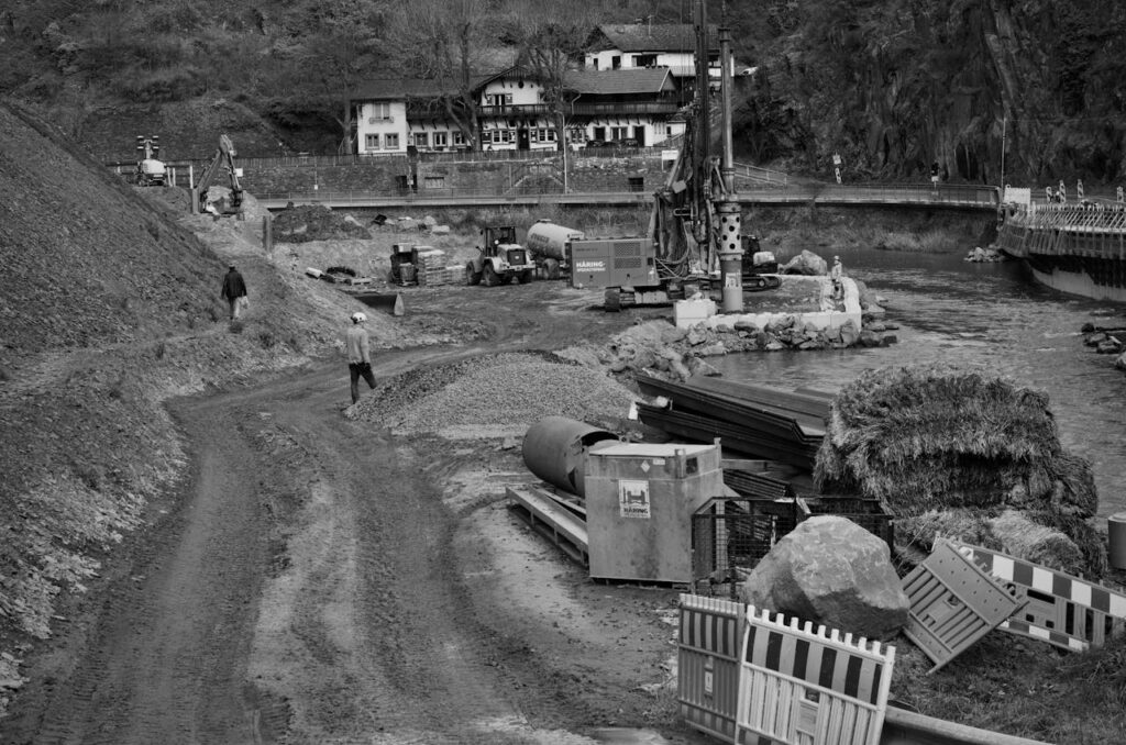 Monochrome image of construction site next to a river with heavy machinery and workers.